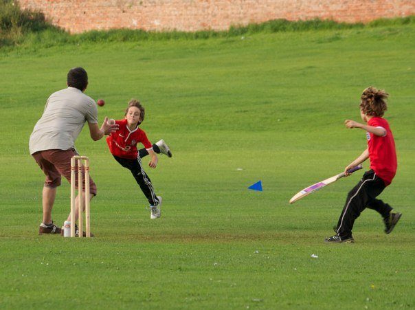 Child cricketer diving and throwing a ball at the stumps